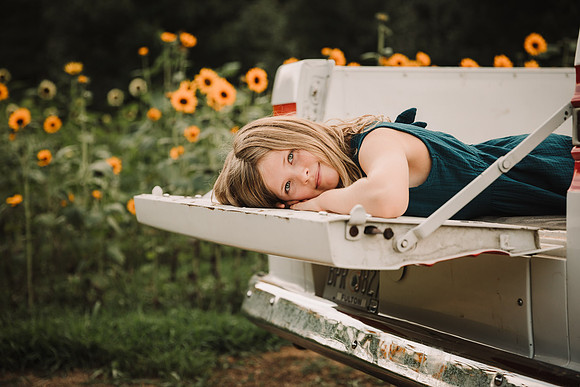 blonde girl laying in a truck bed with sunflowers in the background