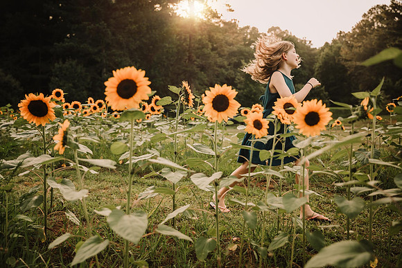 girl happily skipping through a field of sunflowers by monica carlson