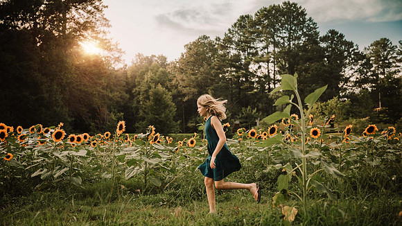 blonde girl running through a sunflower field at sunset