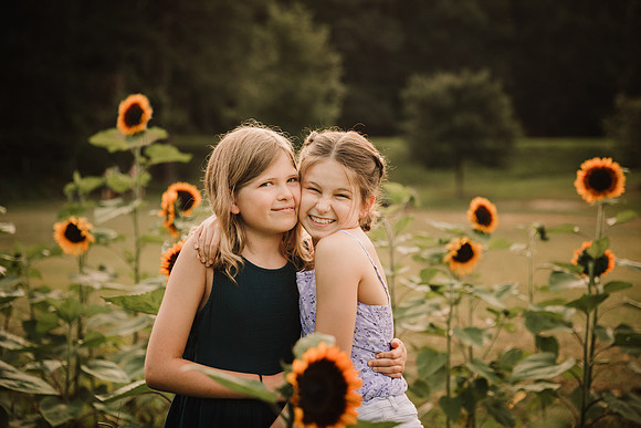 silly sisters huggning on a field of sunflowers in Milton, Ga during a photo session