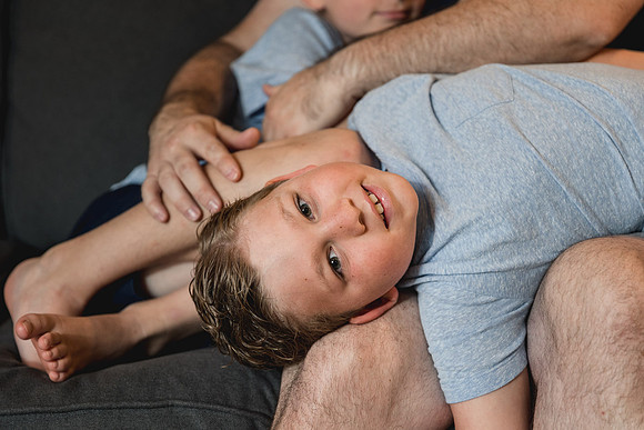 tween boy smiles while liing on his dads lap