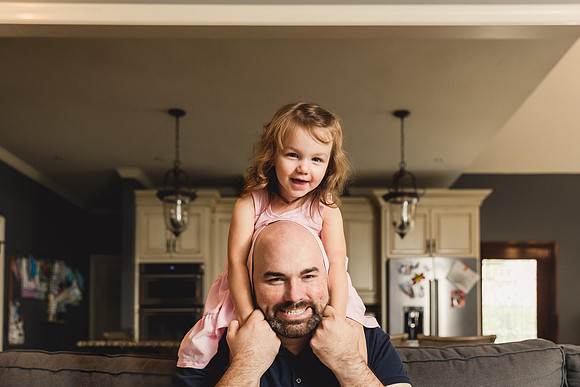 happy daughter sitting on the shoulders of her father by monica carlson