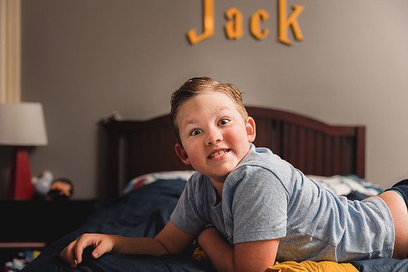 elementary aged boy making a funny face while laying on the bed in his room