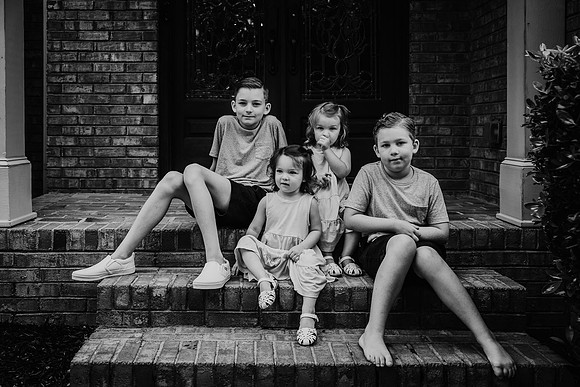 black and white image of four kids sitting on the steps of their home