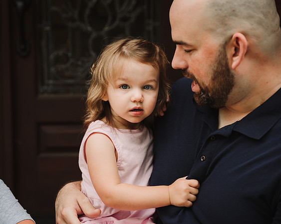 little girl clinging to her father outside their home