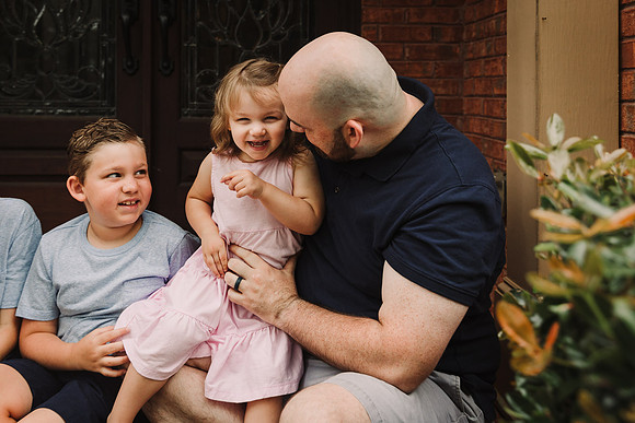 daddy tickles his little girl while his son looks on
