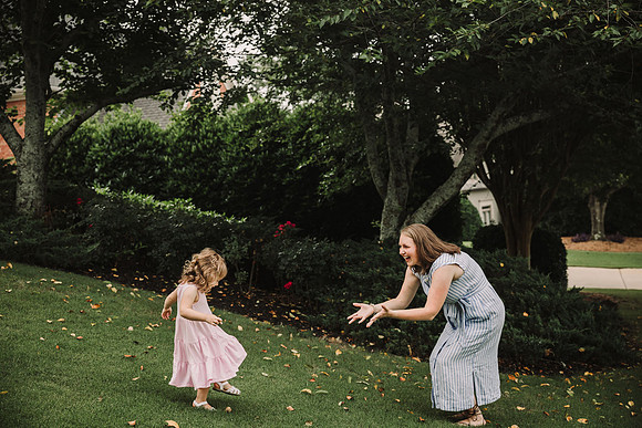 mom smiles as her yound daughter runs to her open arms