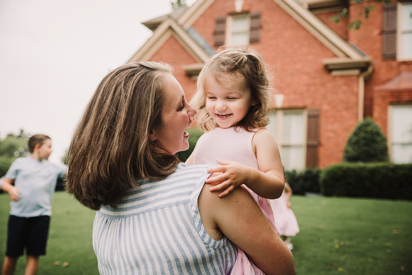 mother happily carries her young daughter outside their home taken by monica carlson