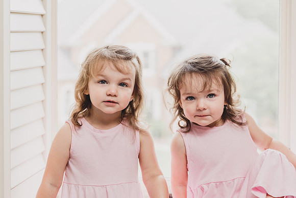 portrait of twin sisters sitting in a window in their room taken during a lifestyle home photo session