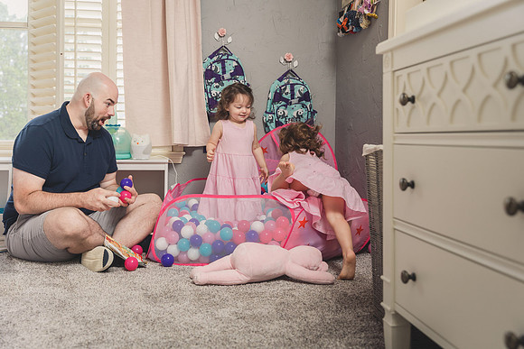 happy father watches his twin toddlers jump into a ball pit in their room