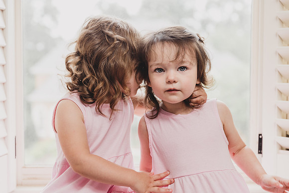 toddler twin girls cuddle in the window of their room