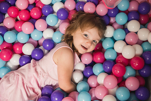 happy little girl looks up at photographer while laying in a ball pit