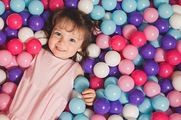 happy toddler girl looks up from a ball pit she is laying in