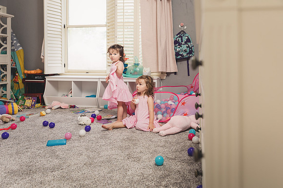 twin girls play on the floor of their messy room during a home photo session