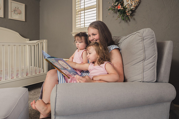 mom snuggles with her daughters in a plush chair to read a book