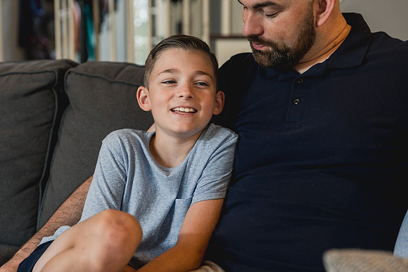 boy giggles while talking to his dad on the couch by monica carlson