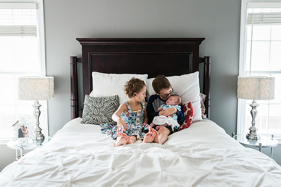 brother and sister holding their newborn sister on a bed