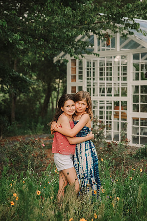 Sisters hugging in a field of flowers behind a greenhouse