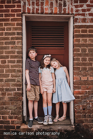 three siblings stand in front of a red door at Barrington Hall
