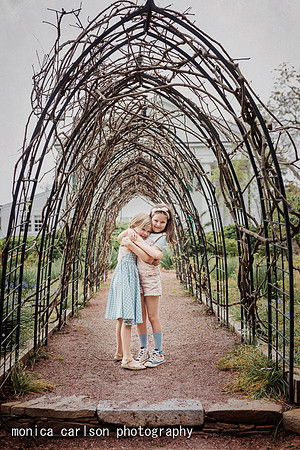 Sisters hugging while standing under a grape vine tunnel