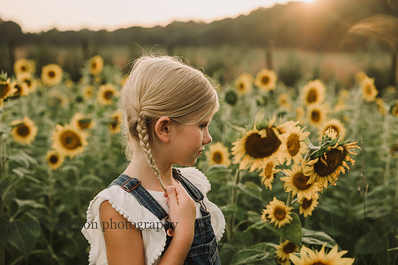 young blonde girl pulls on her braids while she looks at a sunflower