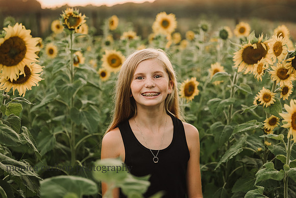 smiling freckled face, red head girl on a sunflower field in Lawernceville