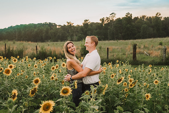husband and wife laugh together on a field of sunflower by monica carlson