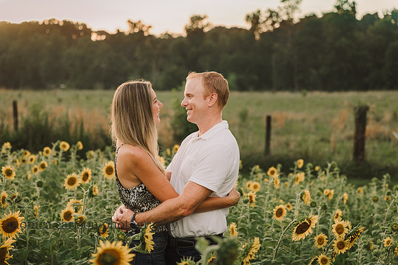 sweet couple hold and look at each other lovinly while standing in a field of sunflowers