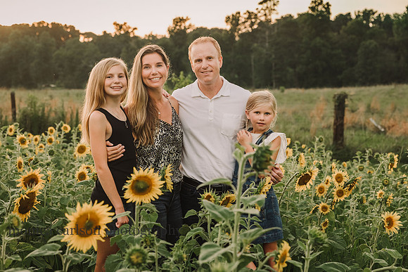 beautiful family of four smile for the camera while surronded by sunflower