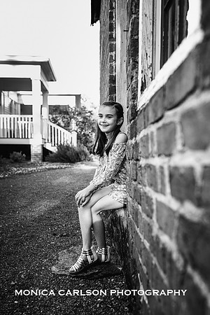 Black and white photo of a happy tween girl sitting in a brick building at a historic property in Roswell, GA