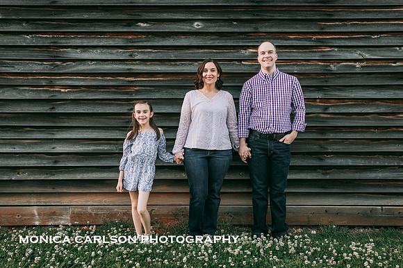 Family of three standing in front of a wooden smoke house at a historic home in Roswell