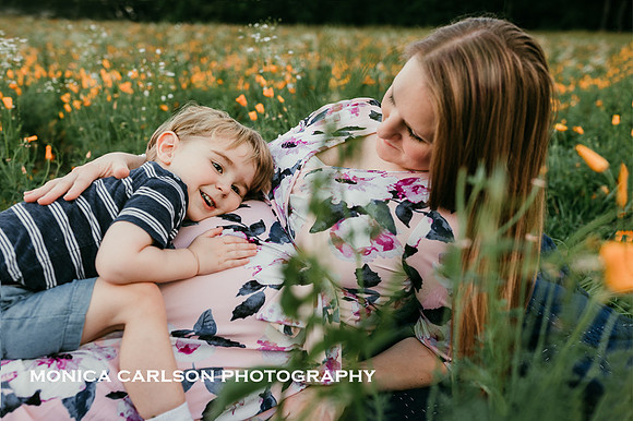 toddler rests his head on his mothers pregnant belly while they lay in a field by monica carlson photography