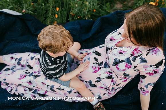 photo from above of a young boy touching his mothers pregnant belly while sitting in a field of flowers