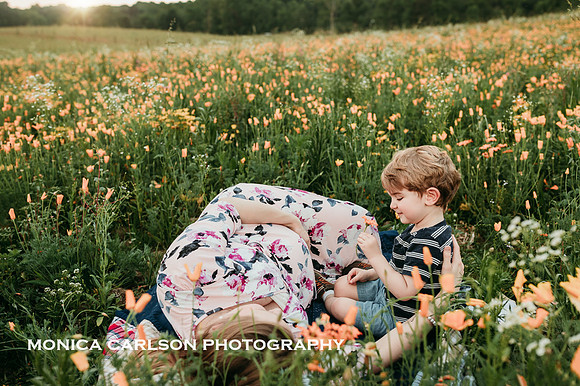 pregnant woman lays in a flower field while her young son looks at the flowers