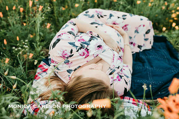 pregnant woman embracing her swollen belly while laying a flower field