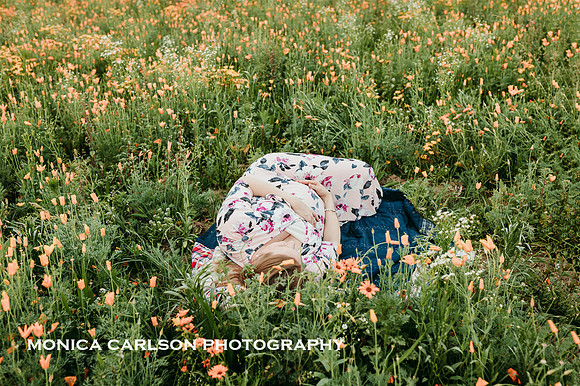pregnant mother lays in a vast wild flower field while holding her belly