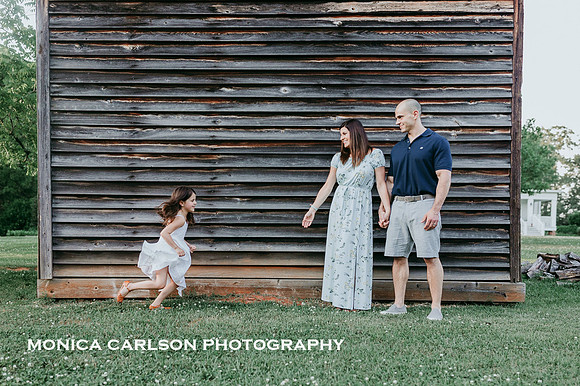 little girl runs to her parents who are standing in front of a wooden smoke house in Roswell