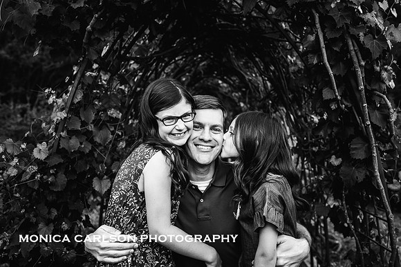 black and white picture of two girls loving on their father by monica carlson