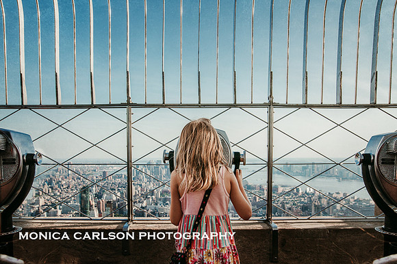 girl looking at New York City through binoculars on the empire state building by monica carlson