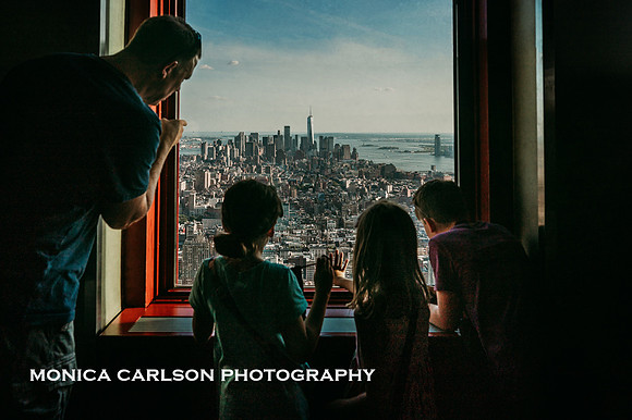 father and his three kids looking at downtown new york city through a window at the empire state building by monica carlson photography