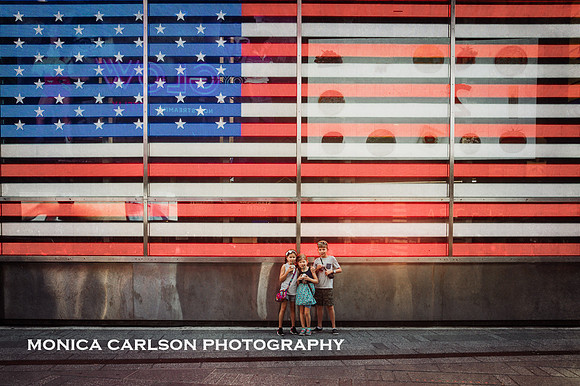 three siblings standing in front of a electronic american flag that is in times square