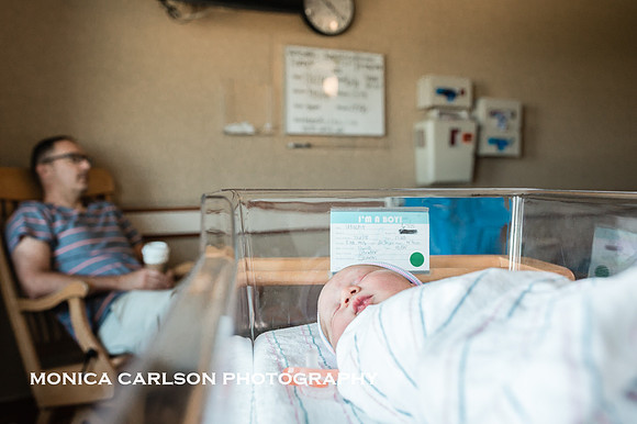 new baby asleep in his hospital bassinet while father sleeps in a chair in the background