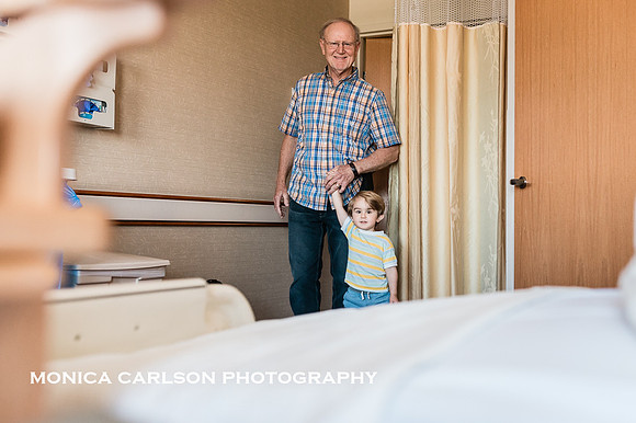 older brother being walked into hospital room by his grandfather to meet his new sibling by monica carlson photography