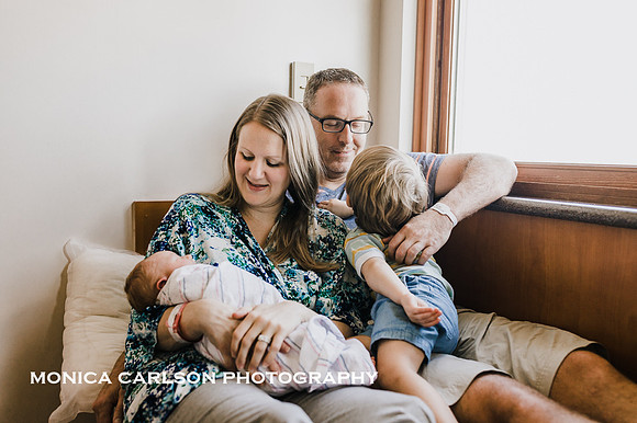 new family of four cuddle together in a hospital room