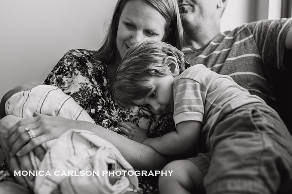 toddler cuddles his mother while she also holds her newborn son by monica carlson