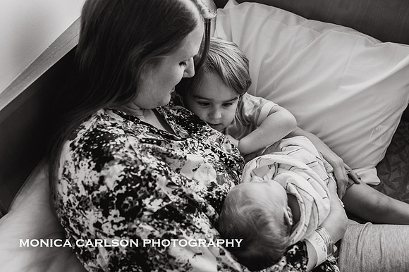 toddler brother watches new sibling while mom hold the fresh baby by monica carlson