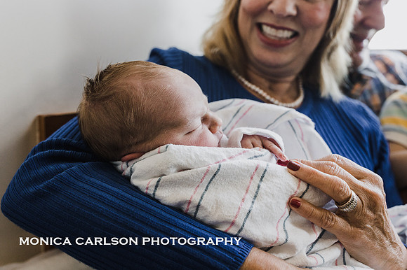 grandmother happily watches newborn grandson sleep in her arms