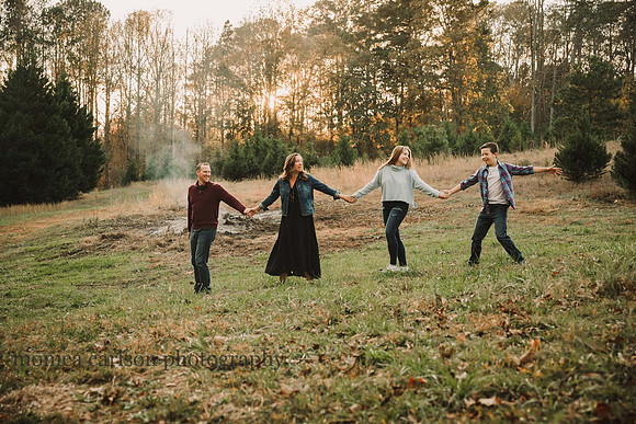 family of four walk together at sunset while a bon fire blows out in the background