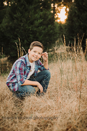 tween boy squats in tall grass at sunset