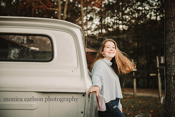 teen girl flips her hair while leaning against a vintage truck